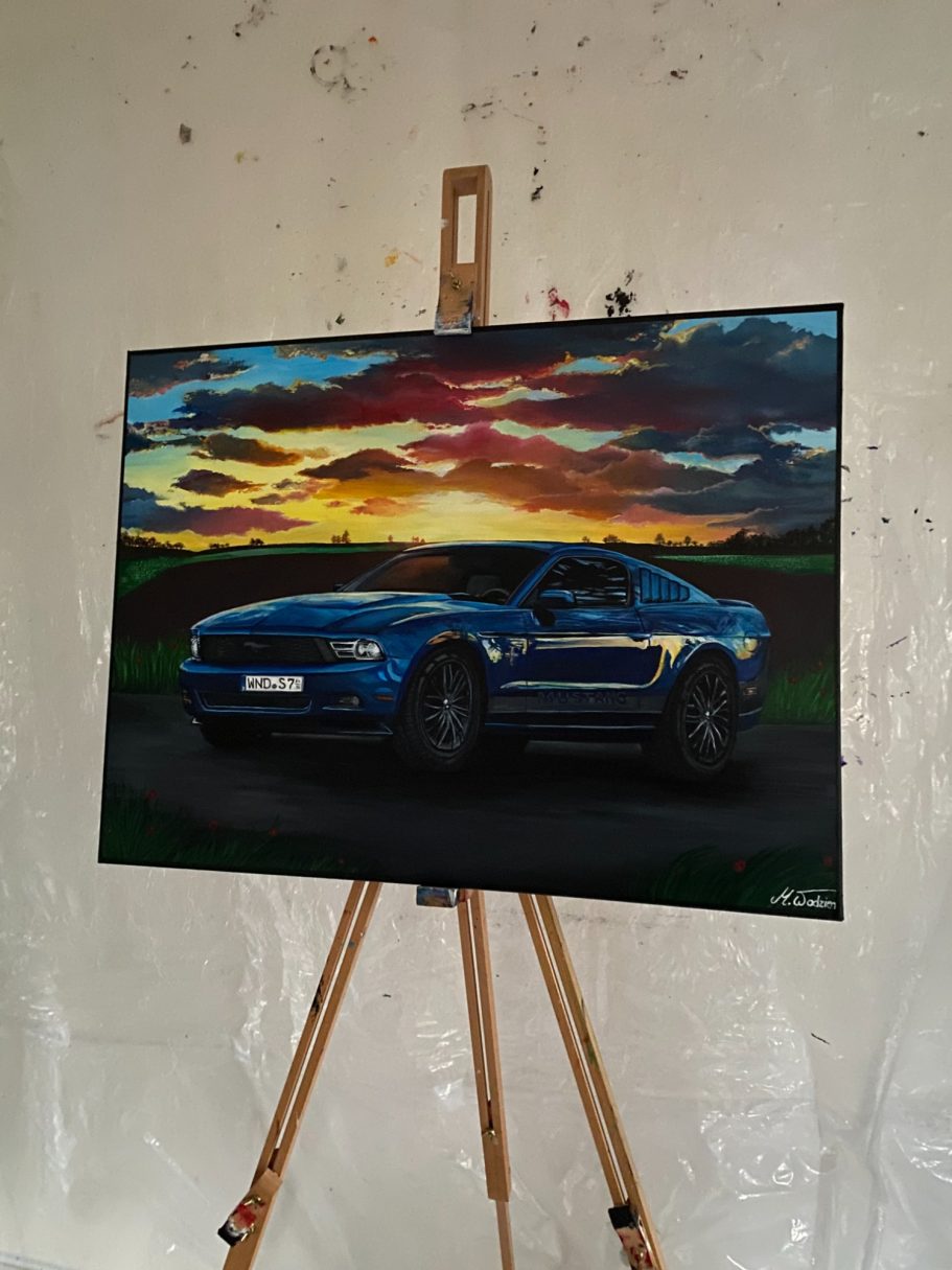 Ein blauer Sportwagen steht vor einer malerischen Landschaft bei Sonnenuntergang.