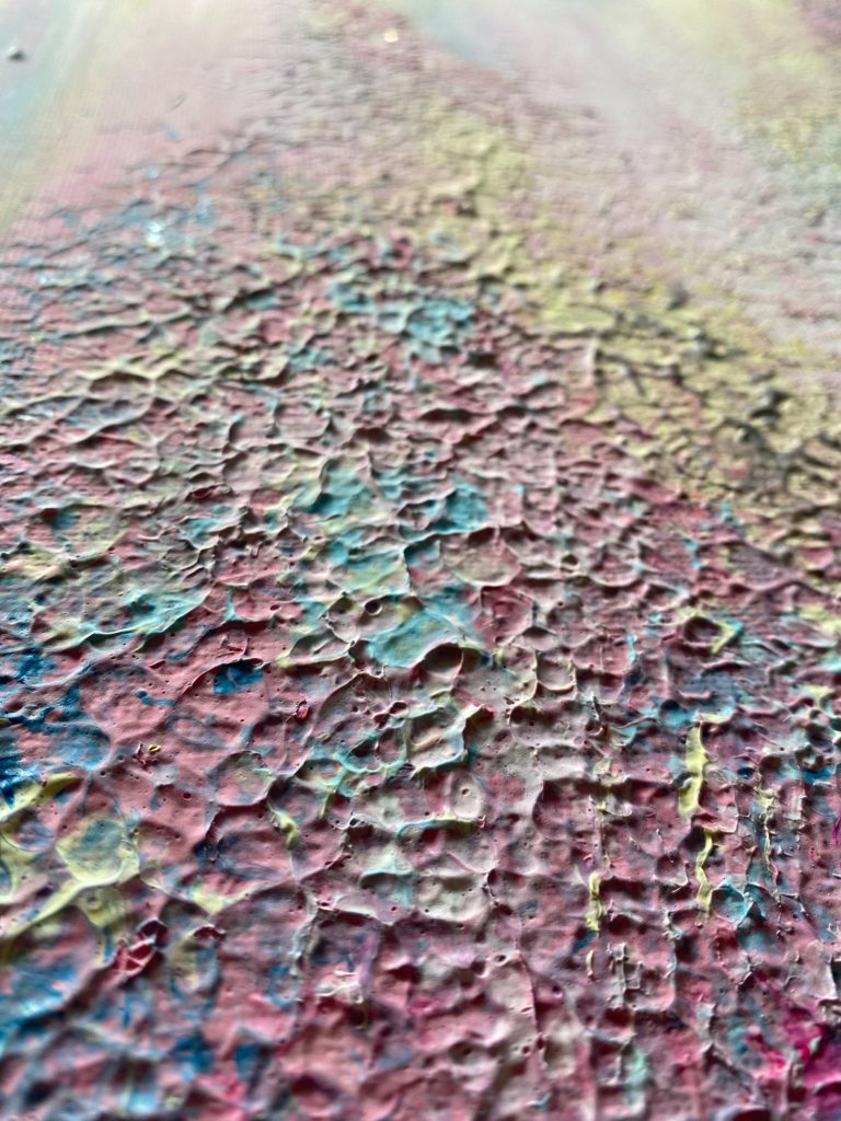 Texturierte Oberfläche mit bunten Farbschichten in Rot, Blau und Gelb.