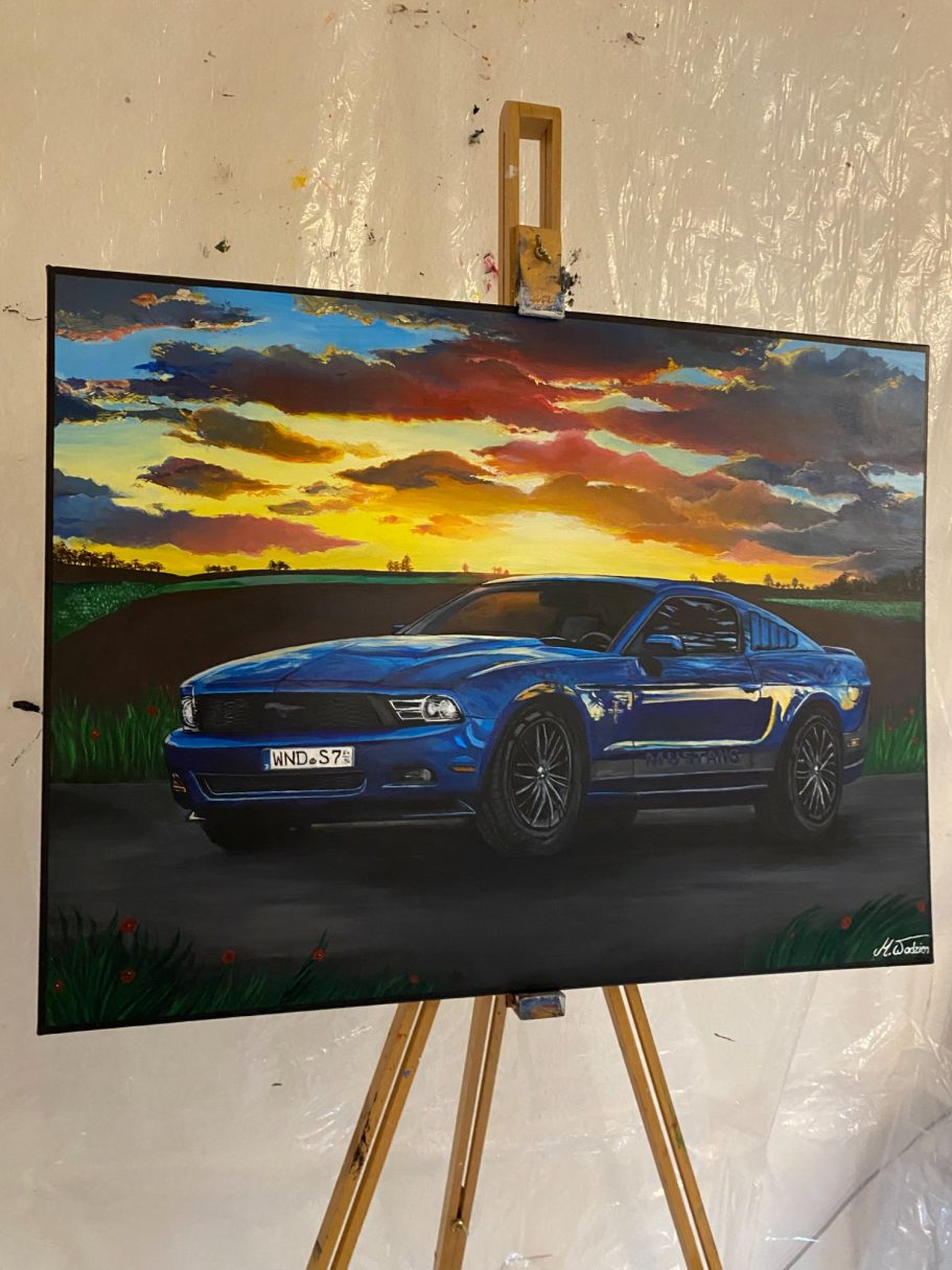 Blauer Mustang vor einem Sonnenuntergang über einer ländlichen Straße.