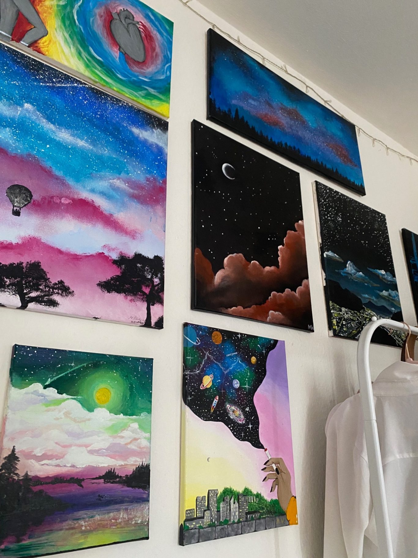 Farbenfrohe Gemälde an einer Wand, die verschiedene Landschaften und Szenen darstellen.