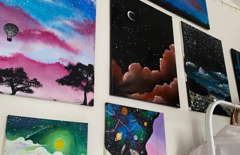 Bunte Acrylgemälde mit Landschaften, Sternenhimmel und Ballonmotiven an einer Wand.