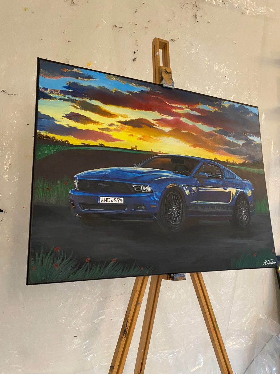 Blaues Auto vor einem Sonnenuntergang, auf einem Ständer in einer Galerie.