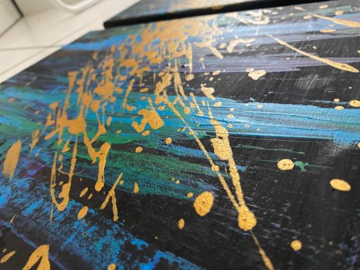 Abstrakte Kunst mit goldenen und blauen Farbsprenkel auf schwarzem Hintergrund.