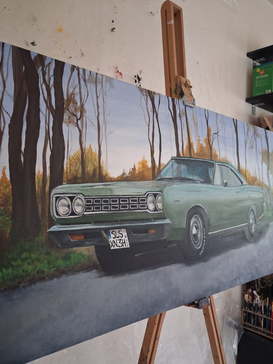 Plymouth Satellite Oldtimer in Grüntönen steht auf einer Straße, umgeben von herbstlichen Bäumen.