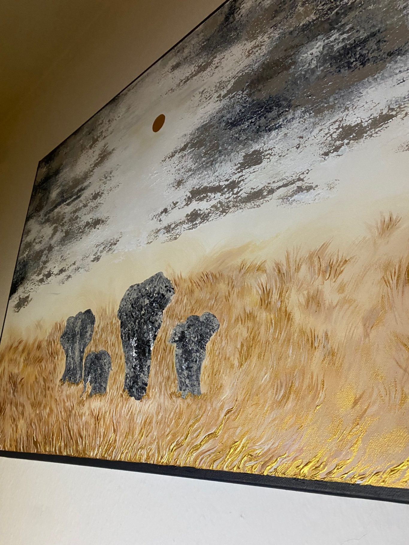 Drei stilisierte Elefanten auf einer Landschaft mit goldenem Gras und einem Sonnenuntergang.