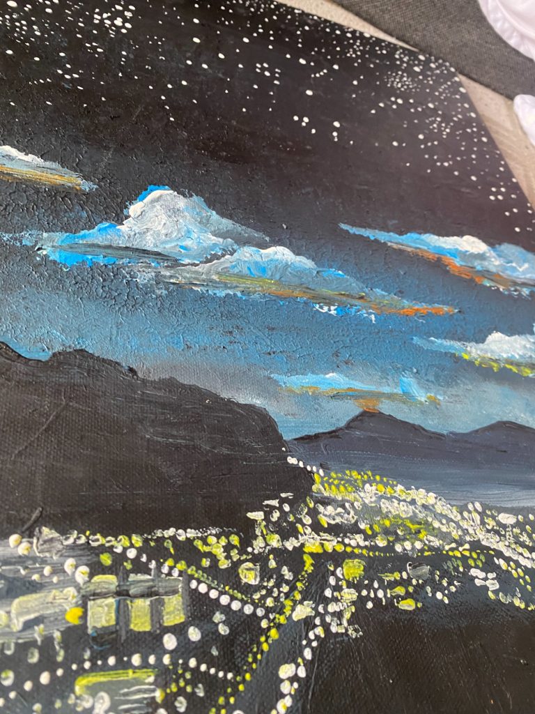 Sternenhimmel über einer Stadt mit Bergen im Hintergrund und leuchtenden Lichtern.