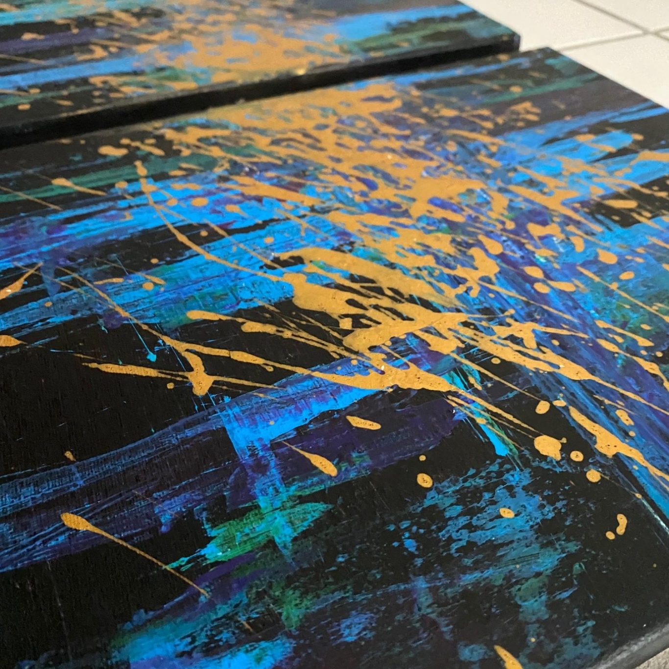 Abstrakte Malerei mit blauen und goldenen Farbspritzern auf schwarzem Hintergrund.